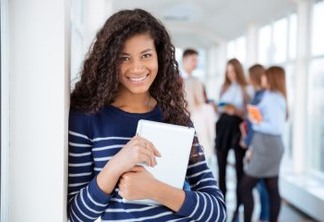 Portrait of a smiling female student standing in university hall with classmates on a background
