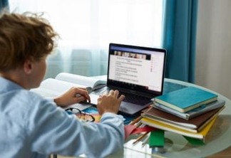 schoolboy is typing report on laptop, do homework. caucasian teen boy engaged in e-learning, looks at screen of laptop