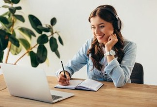 portrait of young smiling woman in headphones taking part in webinar in office