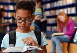 Smart african-american student boy reading book in library, portrait of afro schoolboy preparing for test or exam in school library. Education and knowledge concept