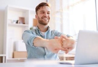 Portrait of handsome young man  stretching at workplace in office and smiling happily, copy space