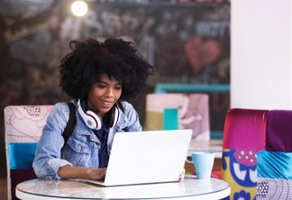 Beautiful young african american student girl with a lot of books and laptop, studying or preparing for exams in a cafe and drink a cup of coffee