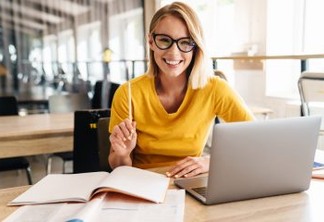 Photo of beautiful happy woman looking at camera while working and sitting at table in open-plan office