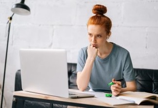Tired redhead young woman is highlighting important things in paper documents. Worried business lady trying find solution of business problem. Focused girl student distance learning at home office.