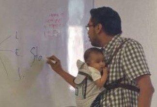 Professor segura bebê para que aluna possa assistir a aula