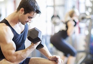Handsome man lifting weight to tone his biceps in a sports gym. A woman is working out her back in the background. Fitness lifestyle, interior shot in a horizontal composition