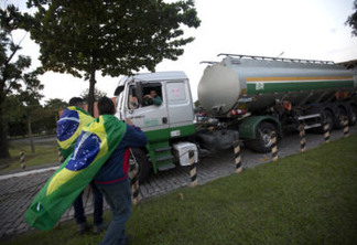 Demonstrators with Brazil's national flag on their shoulders stand near a truck loaded with fuel as it leaves the Petrobras refinery in Duque de Caxias, Brazil, Friday, May 25, 2018. A nationwide strike by thousands of truckers brought much of Latin America's largest nation to a halt on Friday, prompting Brazilian President Michel Temer to authorize the military to use force in removing drivers and their parked vehicles from highways and other roads. (AP Photo/Silvia Izquierdo)