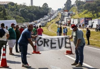 Brazilian truck drivers hold a banner reading "strike" as they block the Regis Bittencourt road, 30 kilometres from Sao Paulo, during the fourth day of strike to protest rising fuel costs in Brazil, on May 24, 2018.  / AFP PHOTO / Miguel SCHINCARIOL