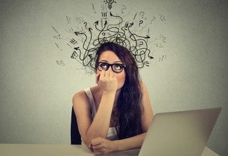Young woman with thoughtful expression sitting at a desk with laptop with lines arrows and symbols coming out of her head