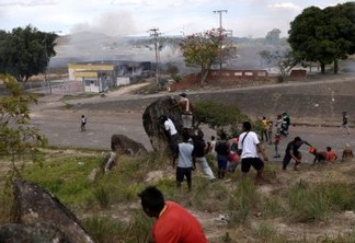 Pessoas se escondem atrás de uma rocha durante confrontos na fronteira venezuelana, em Pacaraima, Brasil 24 de fevereiro de 2019. REUTERS / Ricardo Moraes