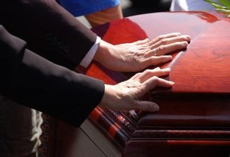 2 hands touching a closed wooden casket.  Farewell to a loved one.