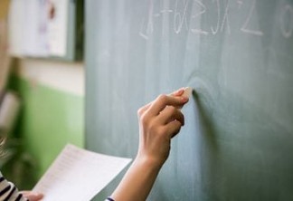 Young female teacher or a student writing math formula on blackboard in classroom.