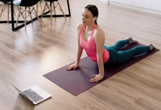 Attractive woman practicing yoga at home using online training instructions