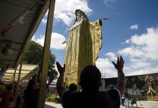 Devotees raise their arms next to a 22-meter-high figure of Saint Death during a ceremony at the International Sanctuary of Saint Death in the municipality of Tultitlan, Mexico state, Mexico, on October 04, 2020. - Mexican devotees have added the protection from COVID-19 in their prayers to Saint Death. (Photo by CLAUDIO CRUZ / AFP)