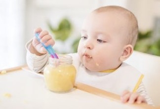A baby grabbing a jar of food while sitting in his high chair