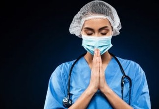 Young female doctor in uniform and with stethoscope making praying gesture isolated over black