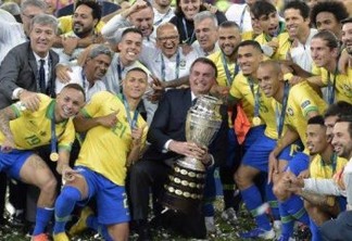 Brazilian President Jair Bolsonaro holds the Copa America trophy as members of the Brazilian national team celebrates after winning the title by defeating Peru in the final match of the football tournament at Maracana Stadium in Rio de Janeiro, Brazil, on July 7, 2019. (Photo by Carl DE SOUZA / AFP)