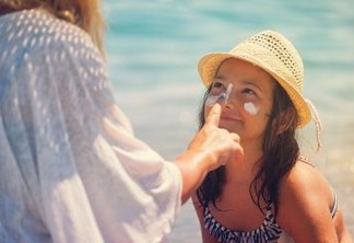 Young mother applying suntan lotion on daughter's face at the beach