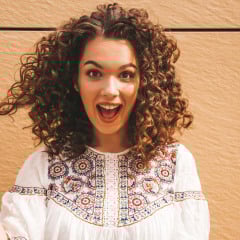 Beautiful smiling model with afro curls hairstyle dressed in summer hipster white dress.Sexy carefree girl posing in street near yellow wall.Funny and positive woman having fun.Shocked and surprised