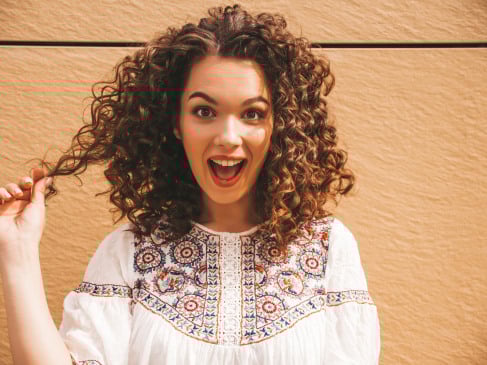 Beautiful smiling model with afro curls hairstyle dressed in summer hipster white dress.Sexy carefree girl posing in street near yellow wall.Funny and positive woman having fun.Shocked and surprised