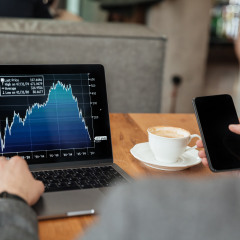 Cropped image of business man sitting by the table in cafe and analyzing indicators on laptop computer while using smartphone