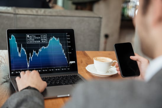 Cropped image of business man sitting by the table in cafe and analyzing indicators on laptop computer while using smartphone